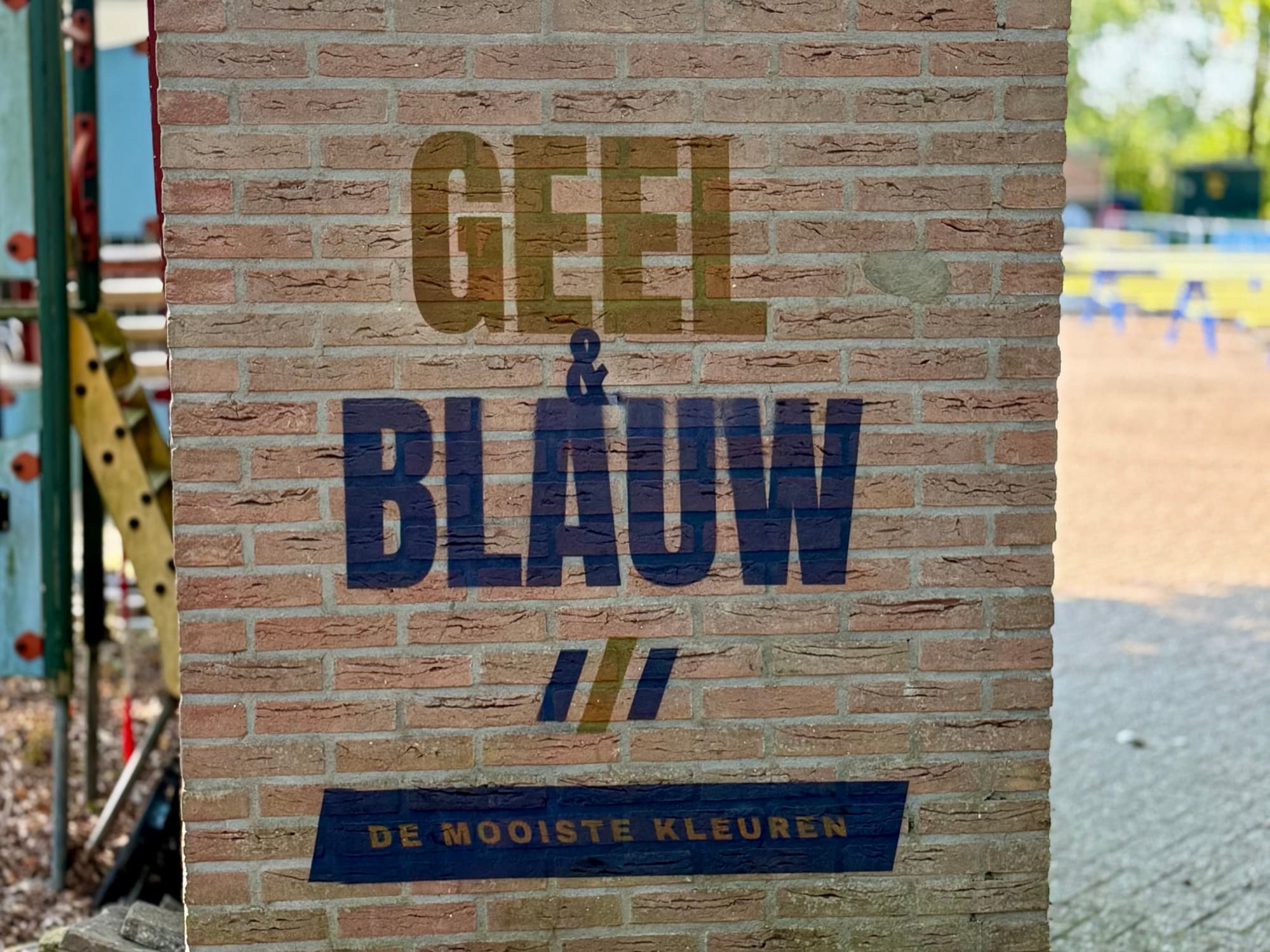 Muurprint met GEEL & BLAUW op de bakstenen buitenmuur van een sportclub